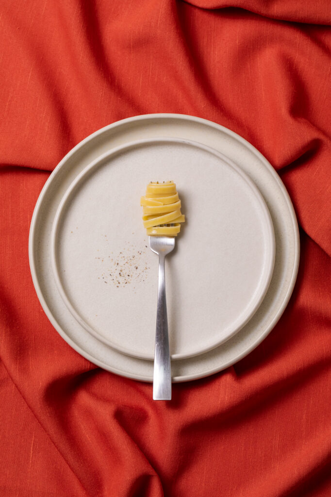Immagine delle Fettucce Mancini avvolte in una forchetta su piatto che appoggia su un letto di tessuto rosso
